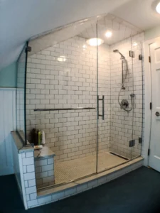 A shower with white subway tiles and a stone bench, enclosed by a floor-to-ceiling frameless glass wall and door.