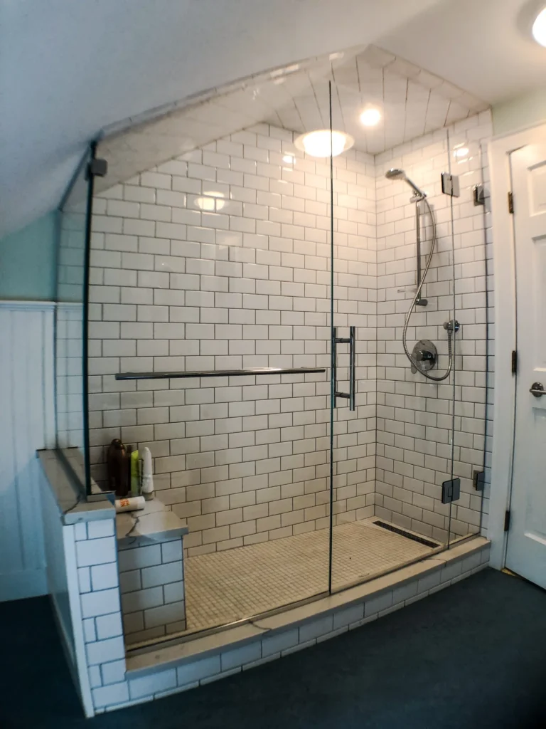 A shower with white subway tiles and a stone bench, enclosed by a floor-to-ceiling frameless glass wall and door.