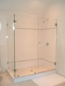 A frameless glass shower enclosure with a light pebble floor and white walls.
