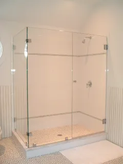 A frameless glass shower enclosure with a light pebble floor and white walls.