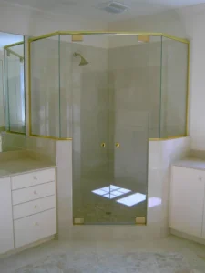 A neo-angle glass shower enclosure featuring decorative gold-toned metal framing and handles.