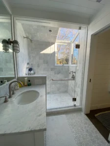 A luxurious marble-tiled shower with a frameless glass door and a large overhead window providing natural light.