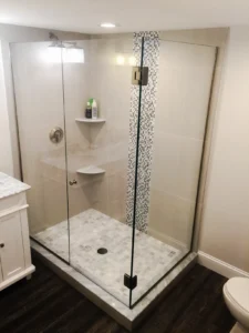 A walk-in glass shower featuring large beige wall tiles and a vertical strip of mosaic glass accents.