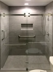 A walk-in shower with grey wood-textured tiles, a sliding glass door system, and a horizontal grab bar.